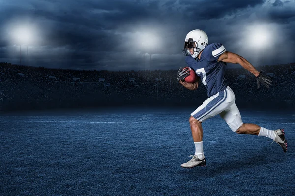 American Football Player Running for a touchdown in a large outdoor professional football stadium at night.