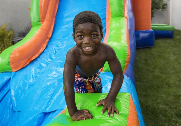 Smiling little boy sliding down an inflatable bounce house. Stock Photo