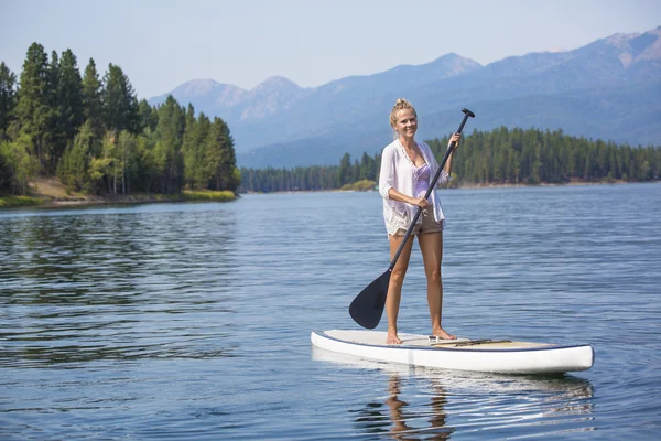 Belle femme pagaie sur le lac de montagne pittoresque. Superbe lac pittoresque et une femme attrayante sur une planche à pagaie . — Photo