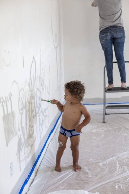 Küçük fırçayla duvarları boyayan şirin bir çocuk.