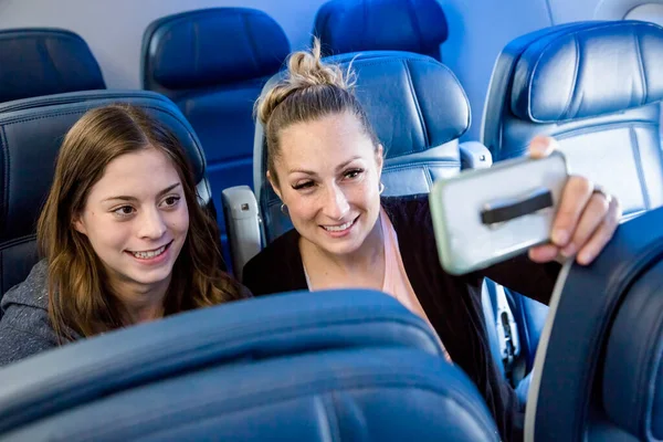 여자가 셀카를 비행기를 중이었습니다 어머니와 비행기에 앉아서 그들의 다가오는 휴가에 — 스톡 사진