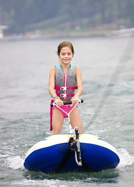 Chica joven montando un tubo de esquí detrás de un barco — Foto de Stock