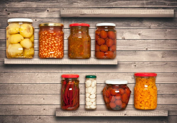 Preserved carrots, tomatoes, garlic, chilli, beans on shelf near a brown wooden wall — Stock Photo, Image