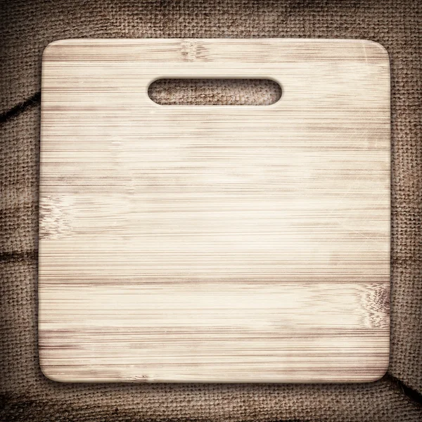 Old cutting board used for cooking on brown crumple burlap tablecloth — Stock Photo, Image