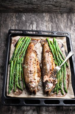 Pişmiş gökkuşağı alabalığı kuşkonmaz ve ahşap masada pişirme tepsisinde baharatlar. 