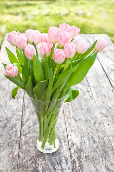 Bouquet of light pink tulips on the oak brown table in a clear g — Stock Photo, Image