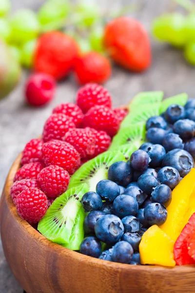 Свіжі барвисті фрукти та ягоди в дерев'яній мисці на сільському столі — стокове фото