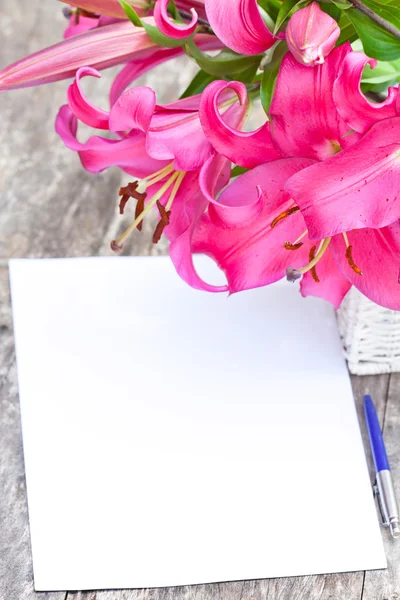 Pink lily Robina flowers bouquet and blank paper sheet with pen — Stock Photo, Image