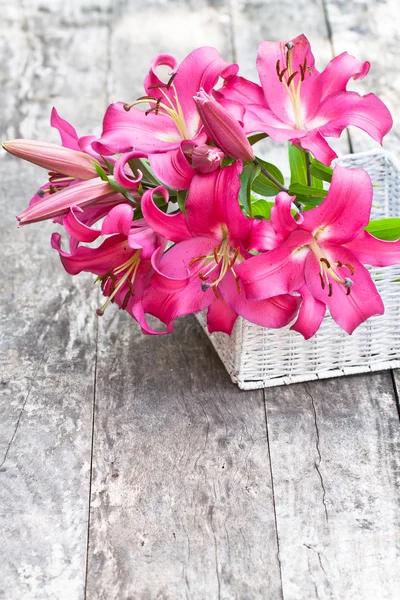 White basket with pink lily flowers bouquet on rustic wooden tab — Stock Photo, Image