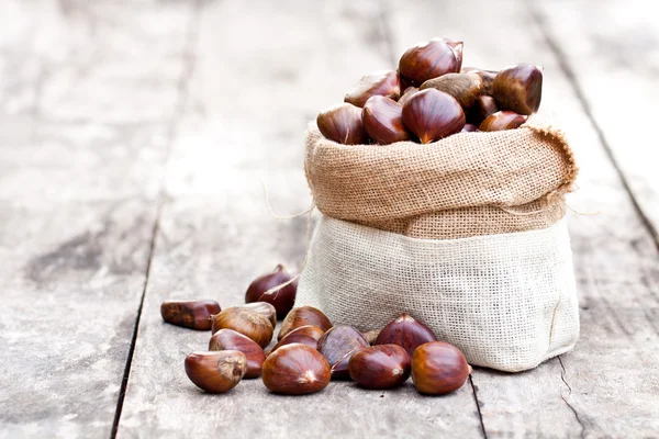 Fresh chestnuts in sack bag on the old wooden table — Stock Photo, Image