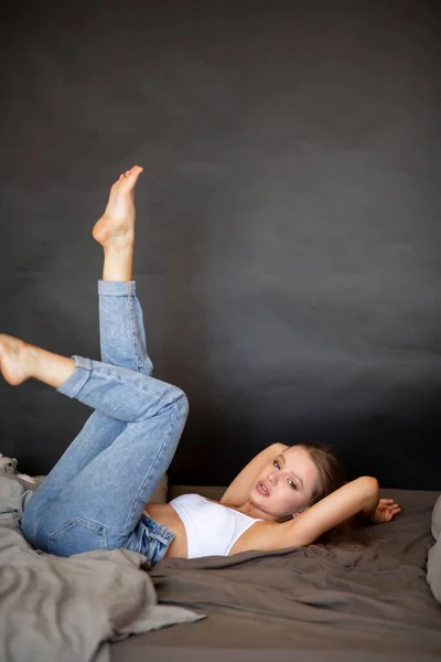 Красива дівчина в джинсах і верх лежить на ліжку з її ногами вгору — стокове фото