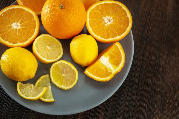 Lemons and oranges on a plate on a dark wooden background