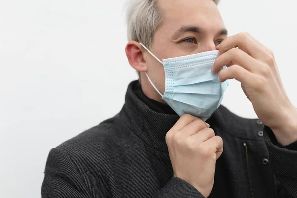 Sokakta beyaz bir arka plana tıbbi maske takan bir adam.