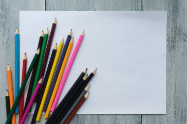 Beyaz tahta zemin üzerinde renkli kalemler olan boş, beyaz bir kağıt yaprağı.
