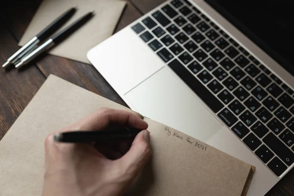 Ein Mann schreibt in ein Notizbuch Meine Pläne für 2021 mit einem Stift auf einem dunklen Holztisch. — Stockfoto
