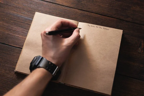 Un hombre escribe en un cuaderno Mis planes para el futuro con un bolígrafo en una mesa oscura. — Foto de Stock