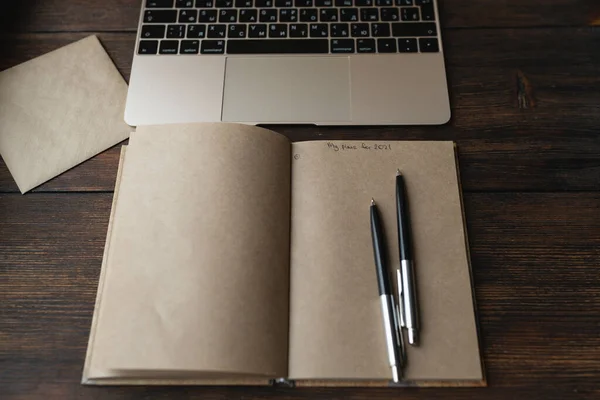 Craft notebook με τις λέξεις Τα σχέδιά μου για 2021 με ένα στυλό σε ένα δίπλα σε ένα φορητό υπολογιστή — Φωτογραφία Αρχείου
