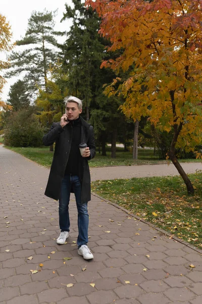 Bir adam sonbahar parkında yürüyor ve telefonda konuşuyor.