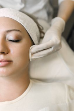 Güzellik uzmanı hastaların cildini pamukla temizliyor.