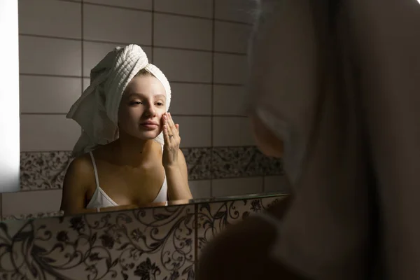 Hermosa mujer caucásica en el baño se aplica crema en la cara después de una ducha. Concepto de cuidado facial de la piel. — Foto de Stock