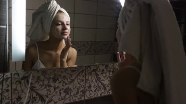 Donna in bagno applica crema dopo una doccia al viso e sorride. — Video Stock