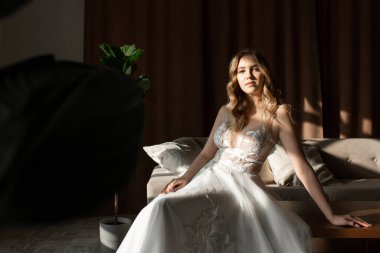 Beyaz gelinlikli bir kadın odada ve kameraya bakıyor.