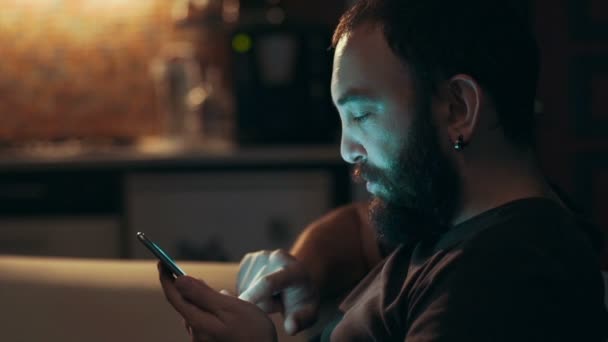 Молодой человек использует свой смартфон в темноте — стоковое видео
