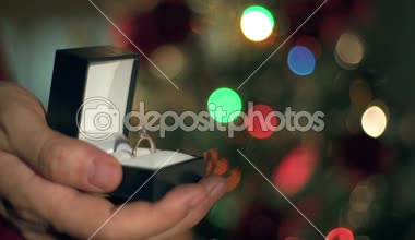 Eller yukarı nişan yüzüğü teklif yakın. Garland yanıp sönüyor. Noel ağacı arka plan