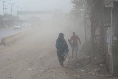 25 Kasım 2020 'de Bangladeş' in Dhaka kentindeki tozlu bir yolda insanlar yürür. Dhaka şehrinin kliması, şehrin pek çok kesimindeki yeni yol inşaatları nedeniyle son iki yıldır endişe verici bir hızla günden güne kötüleşiyor..