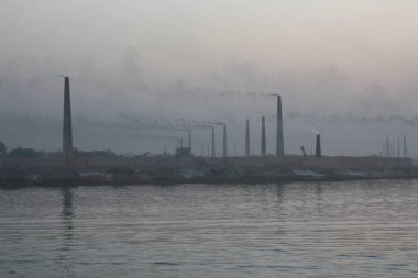 Buriganga Nehri kıyısındaki tuğla fabrikaları. Bu fabrikaların bacalarından çıkan kara duman çevreye ve ekosisteme ciddi bir tehdit oluşturuyor. Dhaka, Bangladeş
