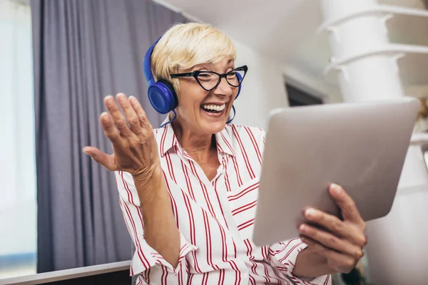 Happy mature woman waving to someone while having a video call over digital tablet at home.