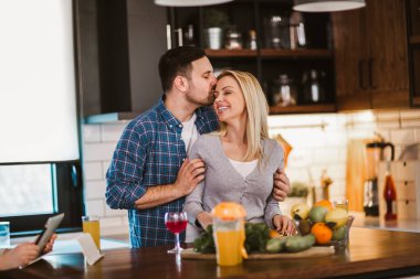 Güzel genç çift evde mutfakta sağlıklı yemekler pişirirken konuşuyor ve gülümsüyor..