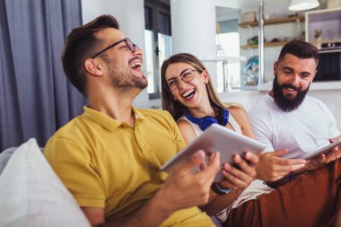 Arkadaşlar evdeki oturma odasındaki koltukta otururken dijital cihazlarını kullanıyorlar.