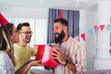 Arkadaşlar arasında doğum gününü kutlayan ve parti yaparken gülümseyen bir grup mutlu insan.