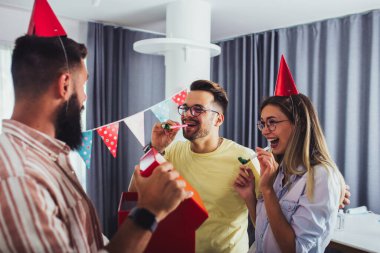 Arkadaşlar arasında doğum gününü kutlayan ve parti yaparken gülümseyen bir grup mutlu insan.