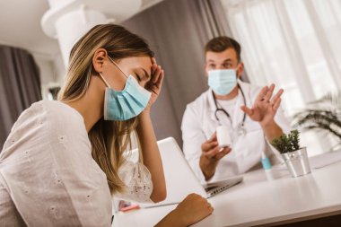 Doktor, sağlık randevusu sırasında koruyucu yüz maskesi takarken hastayla iletişim kuruyor..