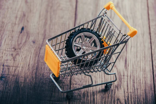 Shopping trolley on wooden table, tyre in the trolley