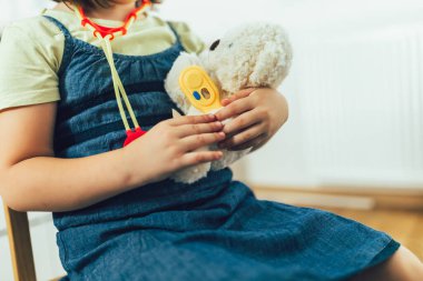 Yumuşak oyuncaklarla doktorculuk oynayan çocuk. Oyuncak ayıyı steteskopla muayene eden kız..