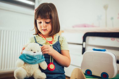 Çocuk ellerinde koruyucu tıbbi maskesi olan yumuşak oyuncak ayı. Yumuşak oyuncakla doktorculuk oynayan çocuk. 