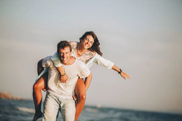 Young man giving piggyback ride to girlfriend on beach.