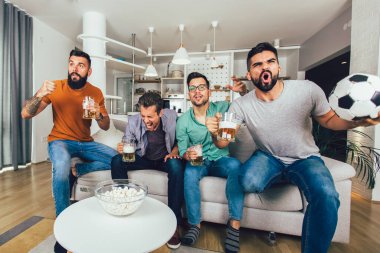 Bir grup futbol taraftarı televizyonda maç izleyip golü kutluyor..