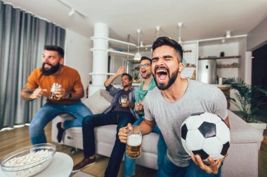 Bir grup futbol taraftarı televizyonda maç izleyip golü kutluyor..