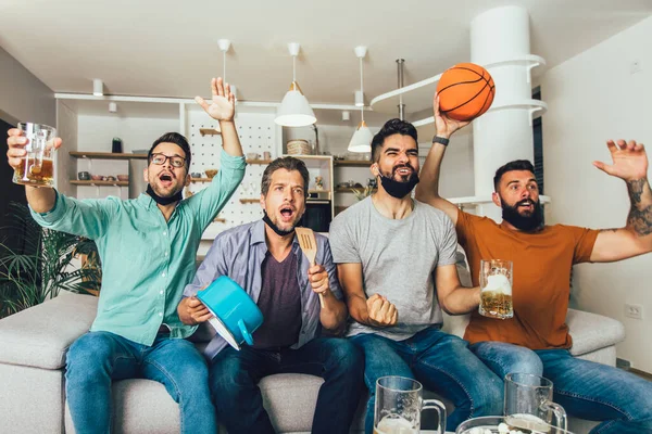 Счастливые Друзья Мужского Пола Защитной Маске Смотрят Баскетбол Дома — стоковое фото