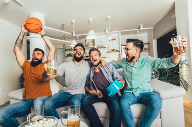 Mutlu erkek arkadaşlar siyah yüz koruyucu maske takıp evde basketbol izliyorlar.