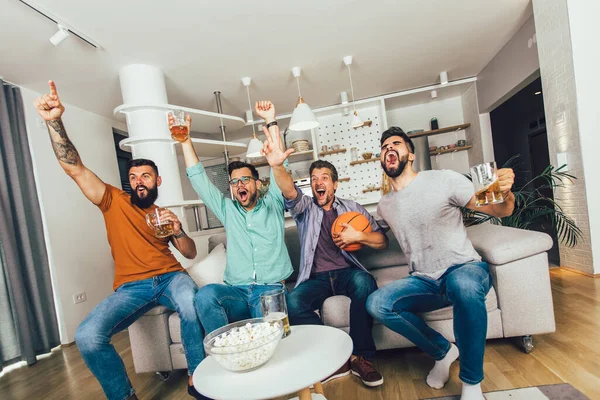 Happy friends or basketball fans watching basketball game on tv and celebrating victory at home.