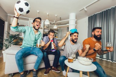 Vuvuzela 'lı mutlu erkek arkadaşlar siyah yüz koruyucu maske takıp evde futbol izliyorlar.