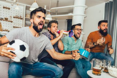Vuvuzela 'lı mutlu erkek arkadaşlar siyah yüz koruyucu maske takıp evde futbol izliyorlar.