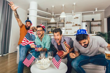 Heyecanlı erkek arkadaşlar evdeki kanepede Amerikan futbolu maçı izlerken tezahürat yapıyorlar..
