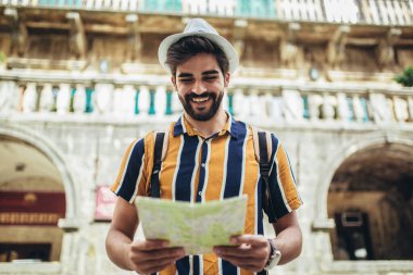 Sırt çantalı mutlu turist şehir genelinde seyahat ederken oryantasyon için bir harita kullanıyor.