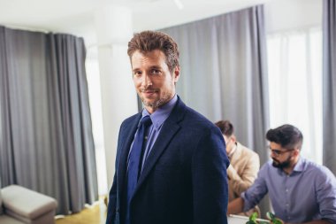 Lider CEO ya da profesyonel işletme koçu arka planda çeşitli mutlu ekiple ofiste poz veren kameraya bakıyor..